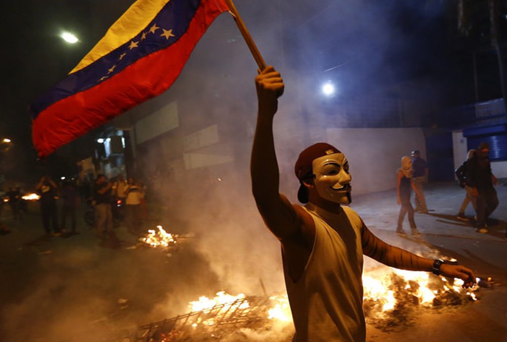homem protestando e segurando a bandeira da Venezuela